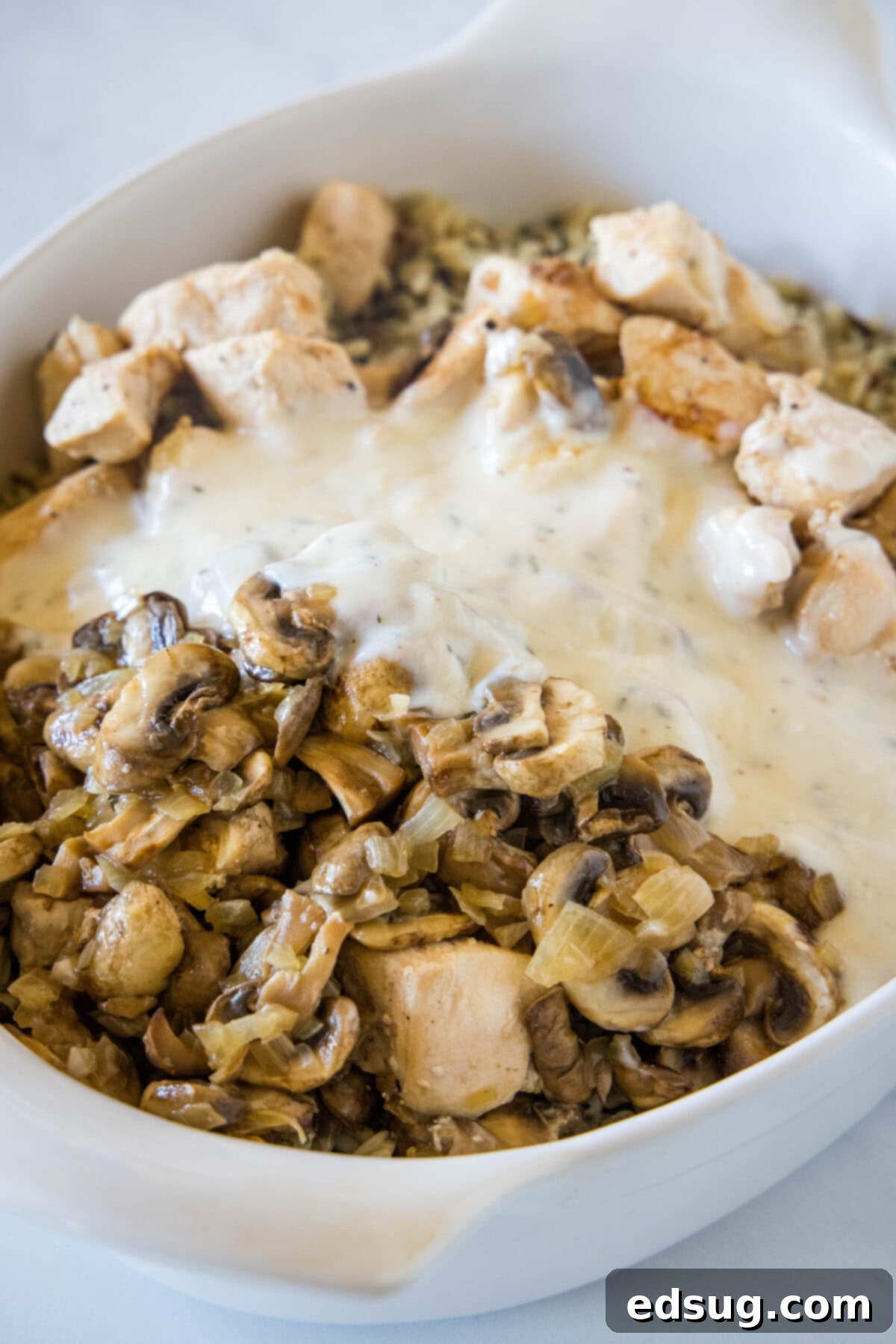 This chicken wild rice casserole is a hearty dinner loaded with juicy chicken, mushrooms, and nutty wild rice wrapped in creamy white sauce. Cream sauce added over top of the chicken and wild rice casserole ingredients in an oval baking dish.