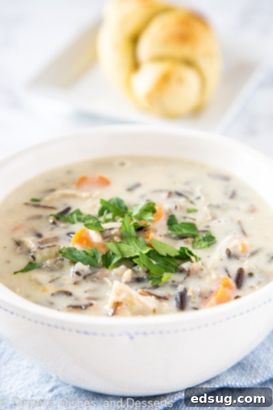 A steaming bowl of creamy chicken wild rice soup garnished with fresh parsley.