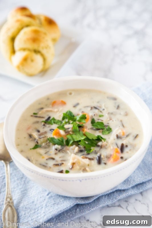 A close-up shot of creamy chicken wild rice soup being scooped with a spoon from a white bowl.