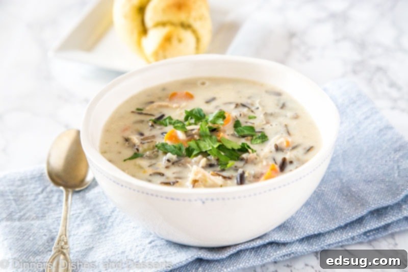 A beautifully presented bowl of creamy chicken and wild rice soup with crusty bread on the side.