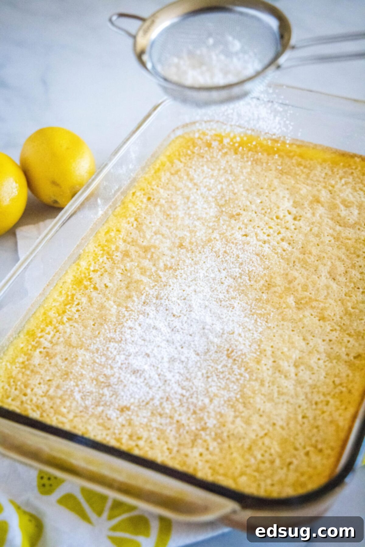 A baking pan full of perfectly baked lemon bars, being dusted with powdered sugar using a sifter