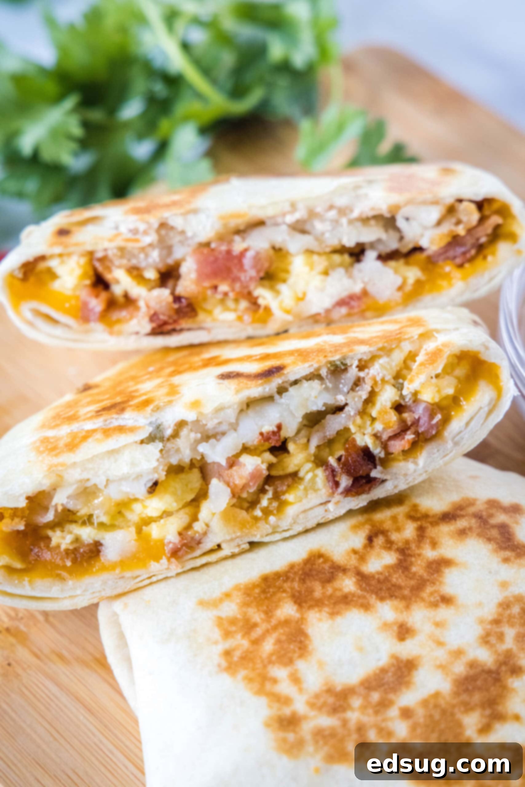 Two halves of a breakfast crunchwrap stacked on a second whole crunchwrap on a wooden cutting board, highlighting the savory layers.