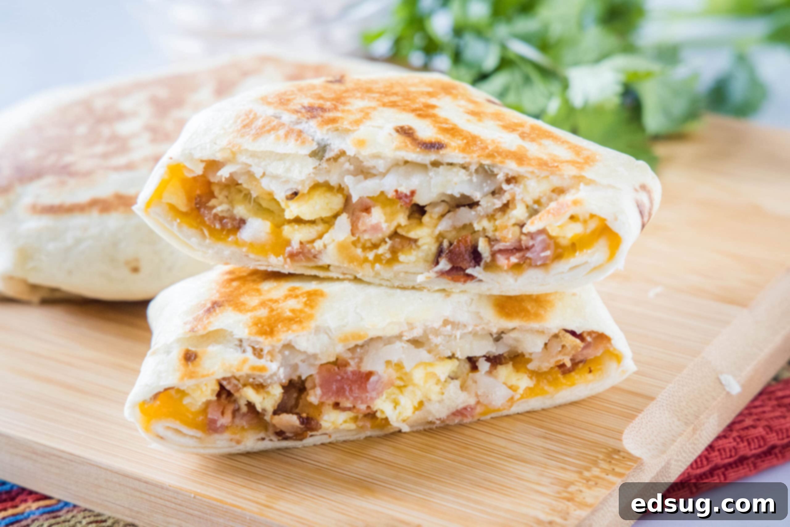 Two halves of a breakfast crunchwrap stacked on top of one another on wooden cutting board, garnished for serving.