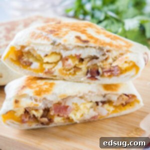 Two halves of a breakfast crunchwrap stacked on top of one another on wooden cutting board, showing the layers.