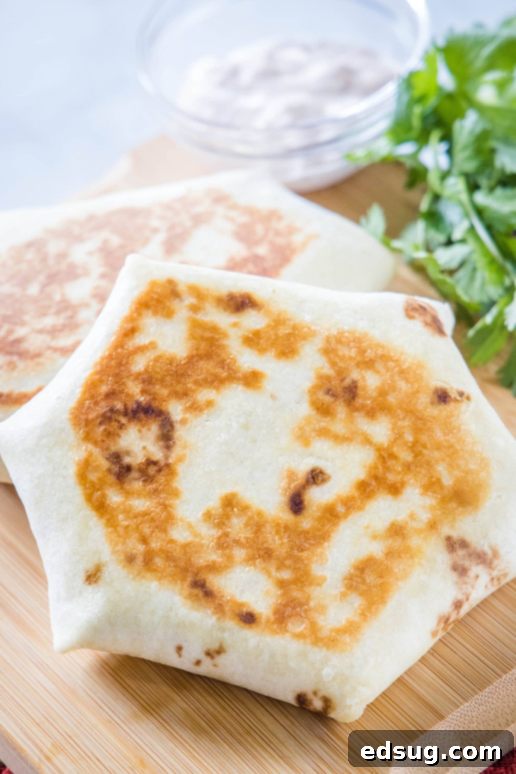A perfectly toasted breakfast crunchwrap propped up against another on a wooden cutting board, ready to be enjoyed.