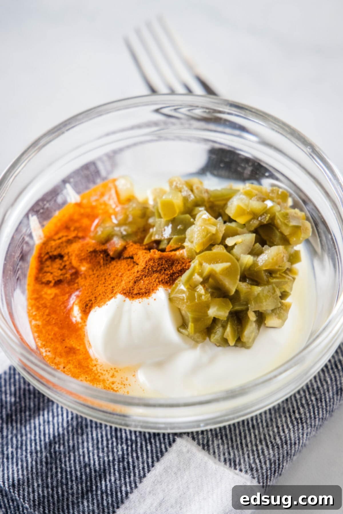 Ingredients for creamy jalapeño sauce combined in a glass bowl, ready to be mixed.