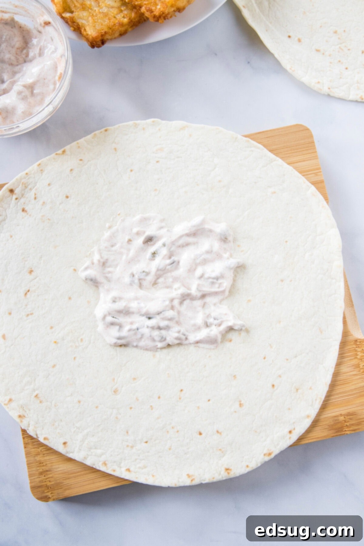 Creamy jalapeño sauce evenly spread in the center of a large flour tortilla, creating the base for the fillings.