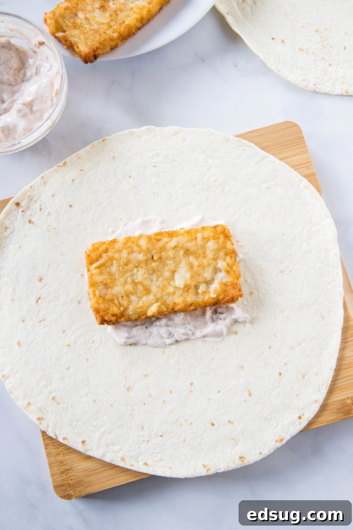 A crispy hashbrown patty layered over creamy jalapeño sauce in the center of a large flour tortilla.