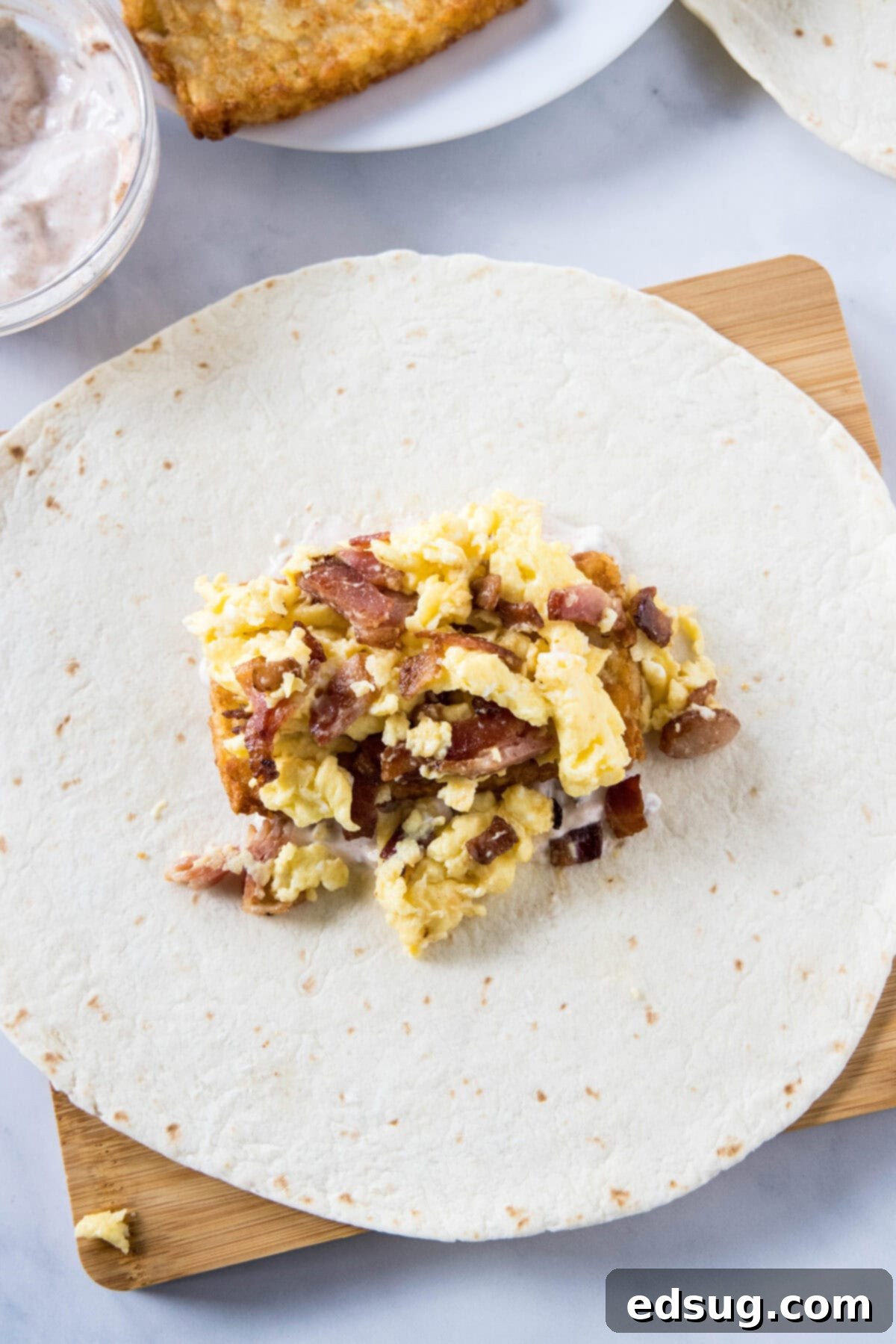 Crunchwrap filling ingredients, including eggs, bacon, and cheese, layered over the hashbrown patty on a flour tortilla.
