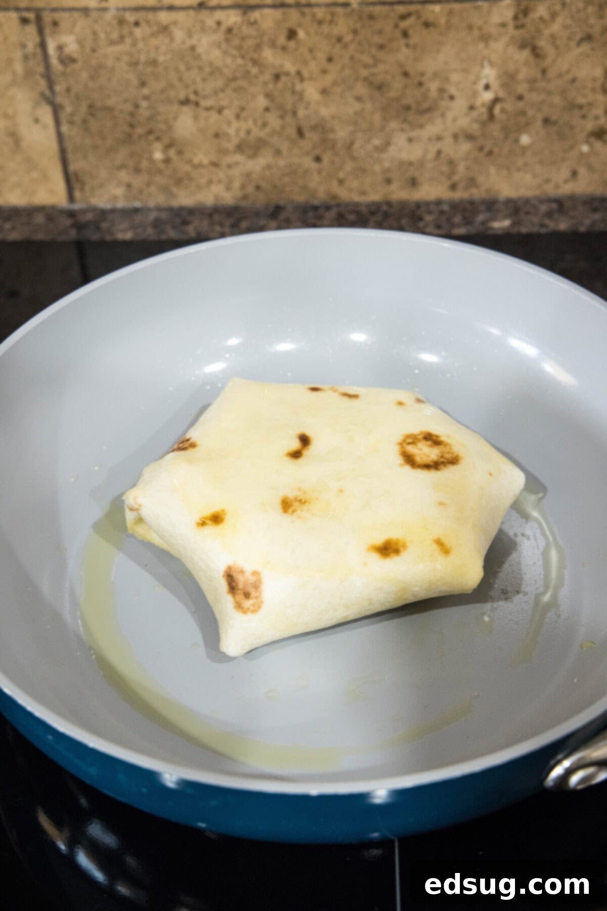 A perfectly folded breakfast crunchwrap cooking seam-side down in a hot skillet, achieving a golden-brown crust.