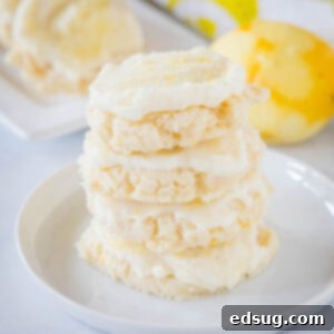Four frosted lemon sugar cookies stacked on a plate with a zested lemon in the background.