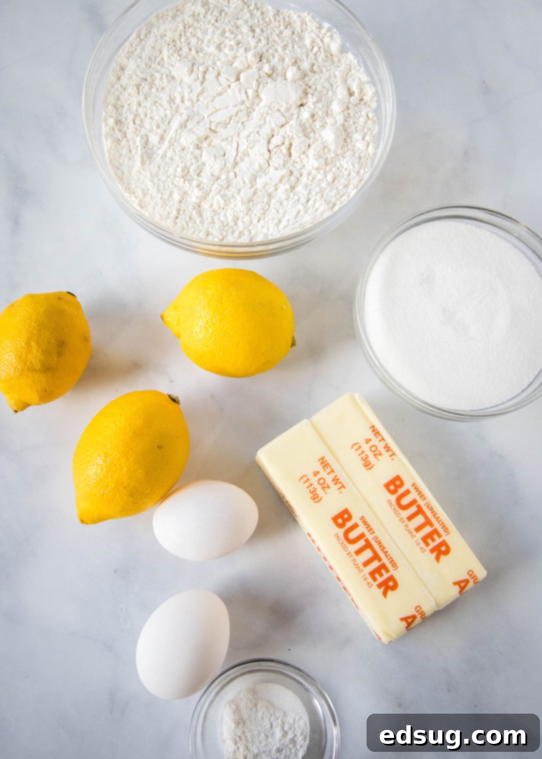 Soft lemon sugar cookies put a bright, zesty spin on a classic recipe! Made from real lemon juice and zest, topped with creamy lemon frosting.  A vibrant display of fresh ingredients for lemon sugar cookies, including bright yellow lemons, softened butter, and eggs, arranged beautifully on a countertop.