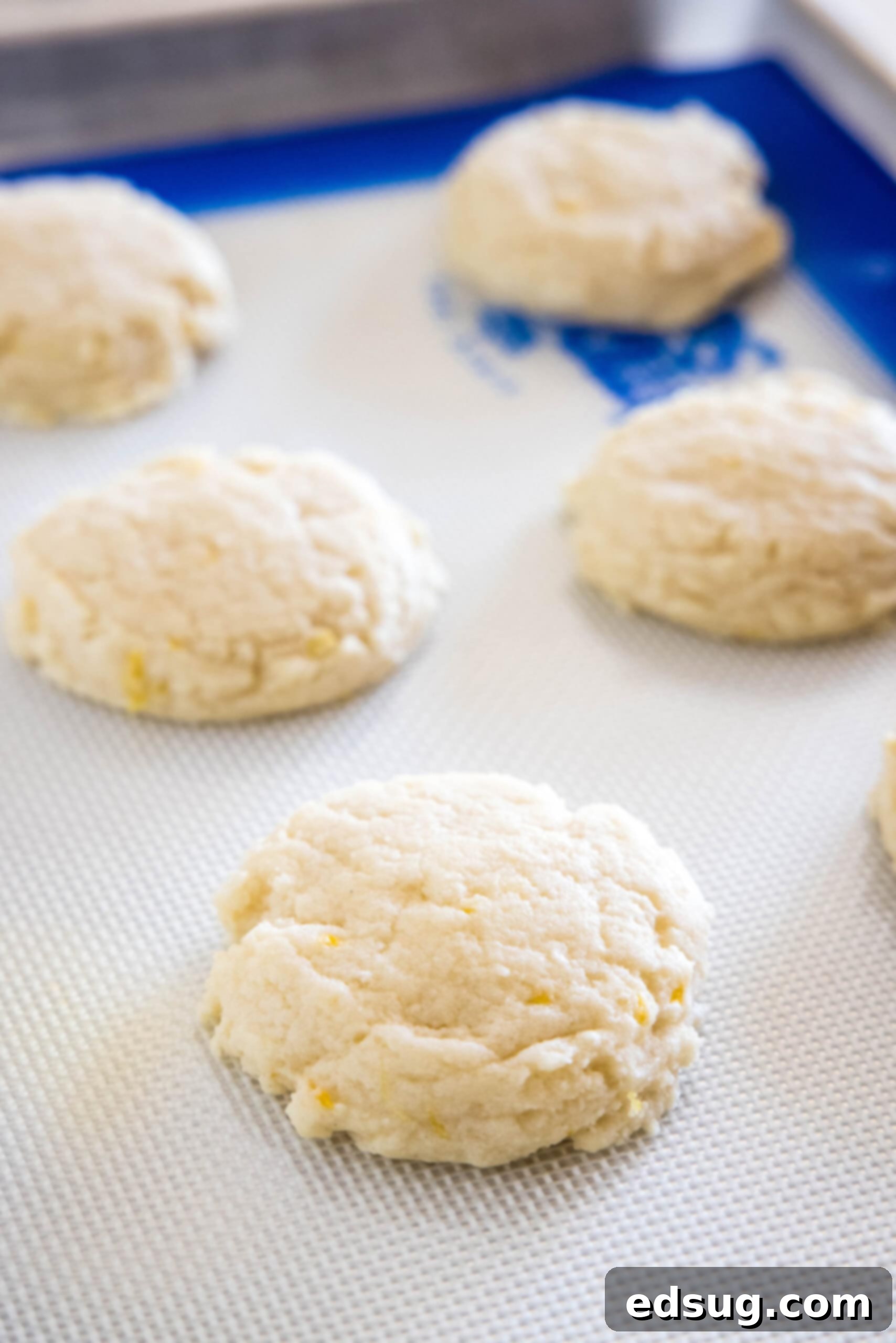 Soft lemon sugar cookies put a bright, zesty spin on a classic recipe! Made from real lemon juice and zest, topped with creamy lemon frosting.  Freshly baked lemon sugar cookies, golden brown at the edges and perfectly set, cooling on a silpat-lined baking sheet, ready for frosting.