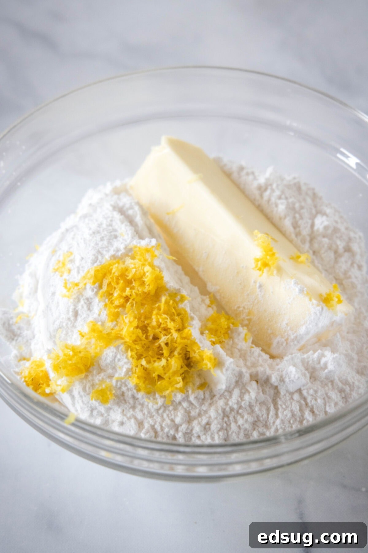 Soft lemon sugar cookies put a bright, zesty spin on a classic recipe! Made from real lemon juice and zest, topped with creamy lemon frosting.  Ingredients for creamy lemon frosting, including softened butter, powdered sugar, and fresh lemon zest, gathered in a mixing bowl ready to be combined.