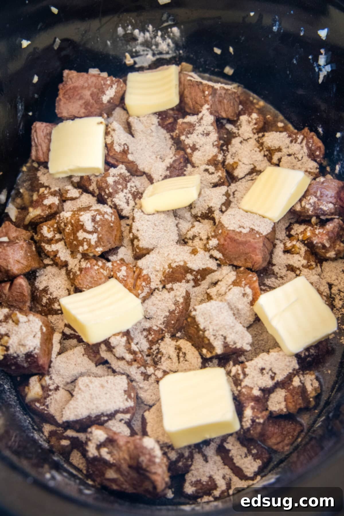 Au jus mix and cubes of butter scattered over steak bites and sauce inside the crockpot.