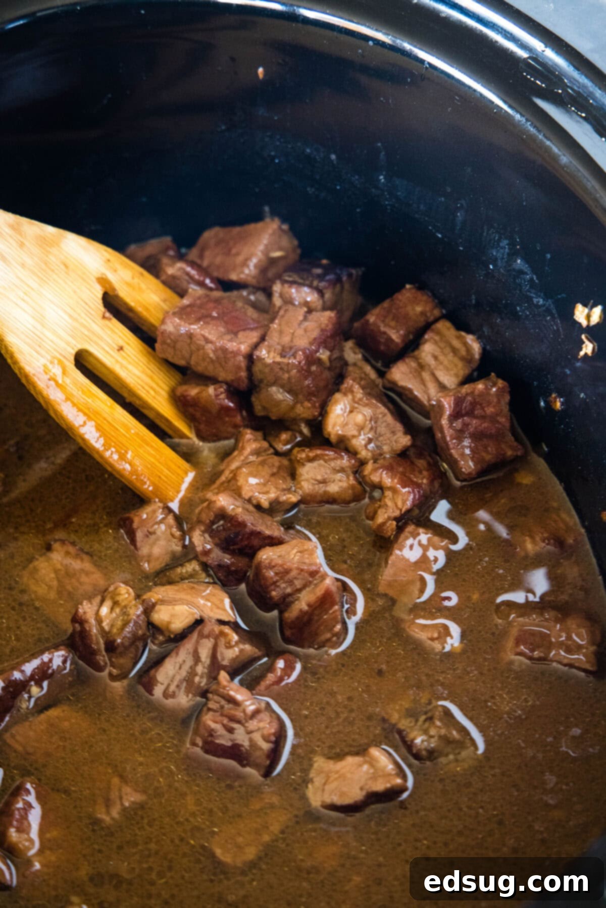 Steak bites and sauce inside the slow cooker with a wooden spoon.