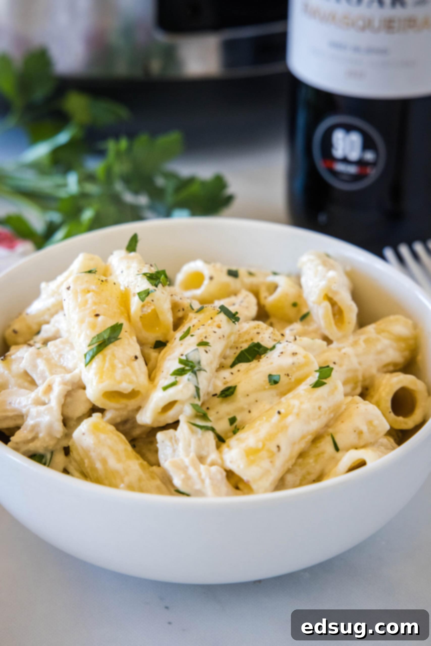 Crock pot chicken alfredo served in a white bowl, garnished with parsley.
