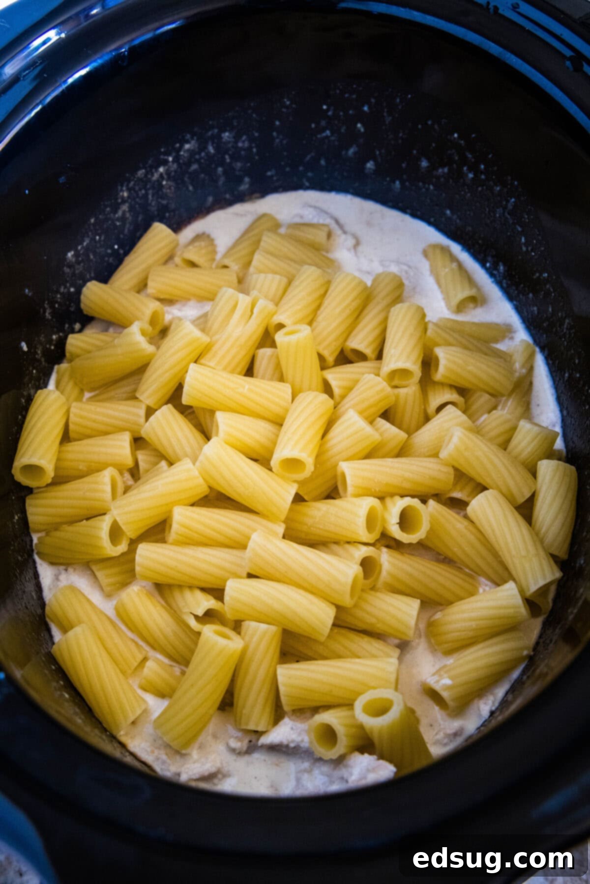 Cooked pasta added to alfredo sauce inside the slow cooker.