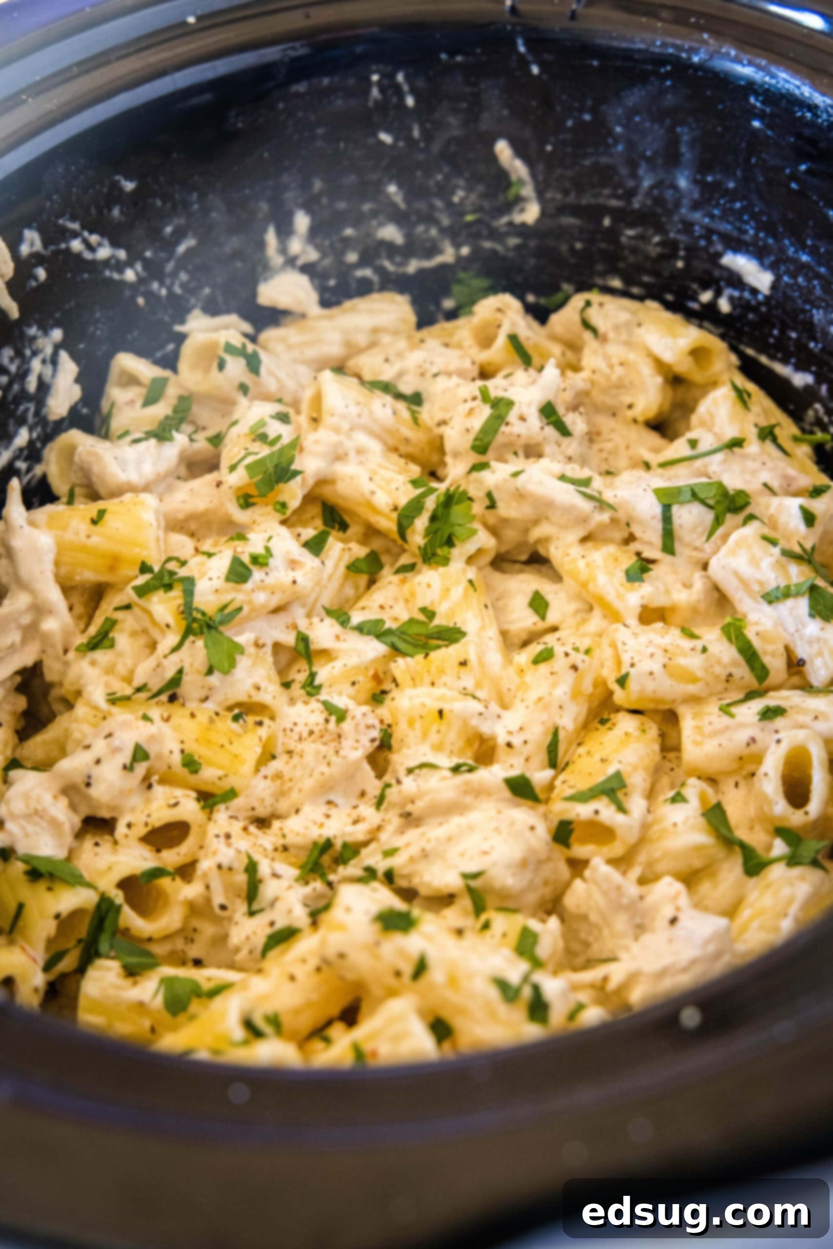 Chicken alfredo inside the crock pot with a spoon stirring it.
