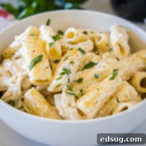 Crock pot chicken alfredo served in a white bowl, garnished with parsley and red pepper flakes.