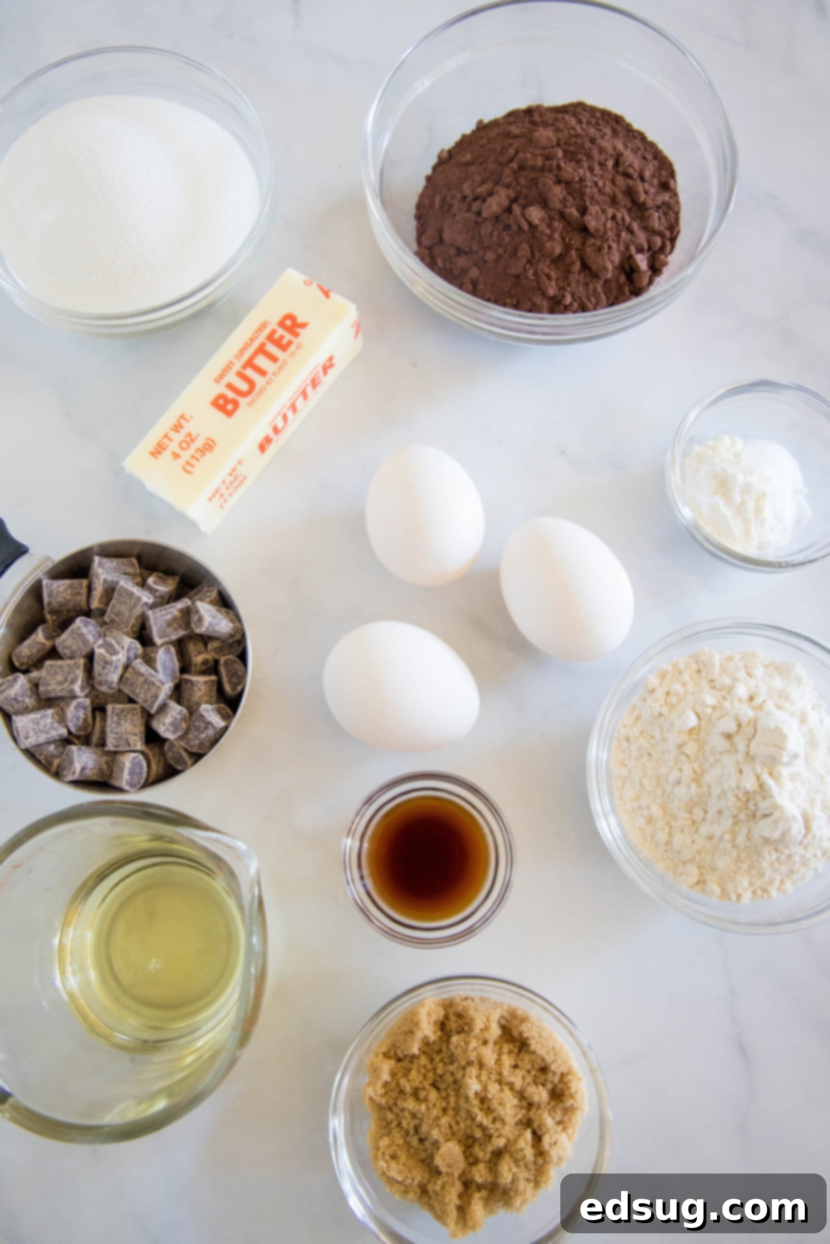 Make thick and chewy, fudgy double chocolate brownies with cocoa powder and chocolate chunks, for loads of melty chocolate in every bite! A beautifully arranged collection of essential ingredients for baking double chocolate brownies, including sugars, butter, eggs, vanilla, cocoa powder, flour, cornstarch, salt, and chocolate chunks, neatly displayed on a rustic wooden surface.