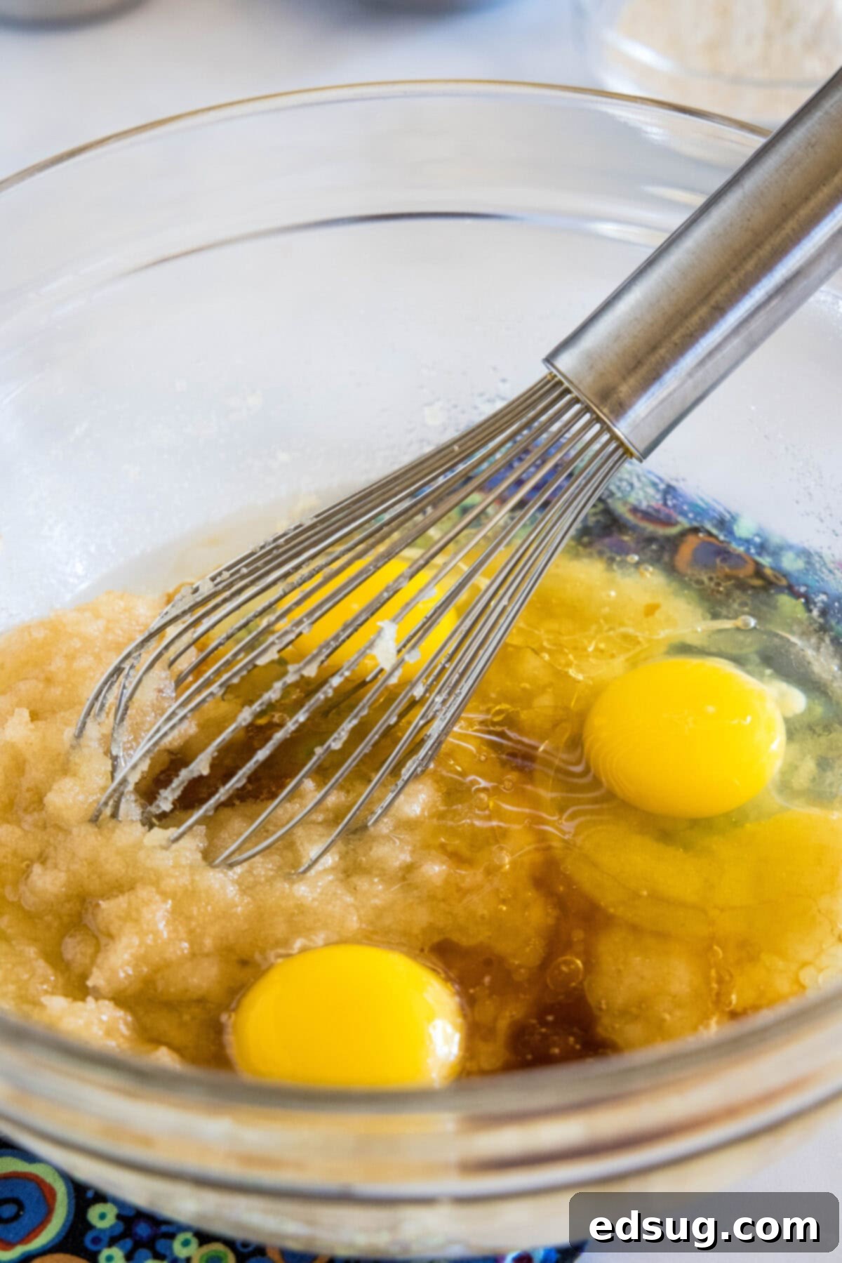 Make thick and chewy, fudgy double chocolate brownies with cocoa powder and chocolate chunks, for loads of melty chocolate in every bite! Large eggs are carefully cracked into a glass mixing bowl containing creamed sugar and melted butter, ready to be whisked together for the brownie batter. The ingredients are perfectly prepped for mixing.