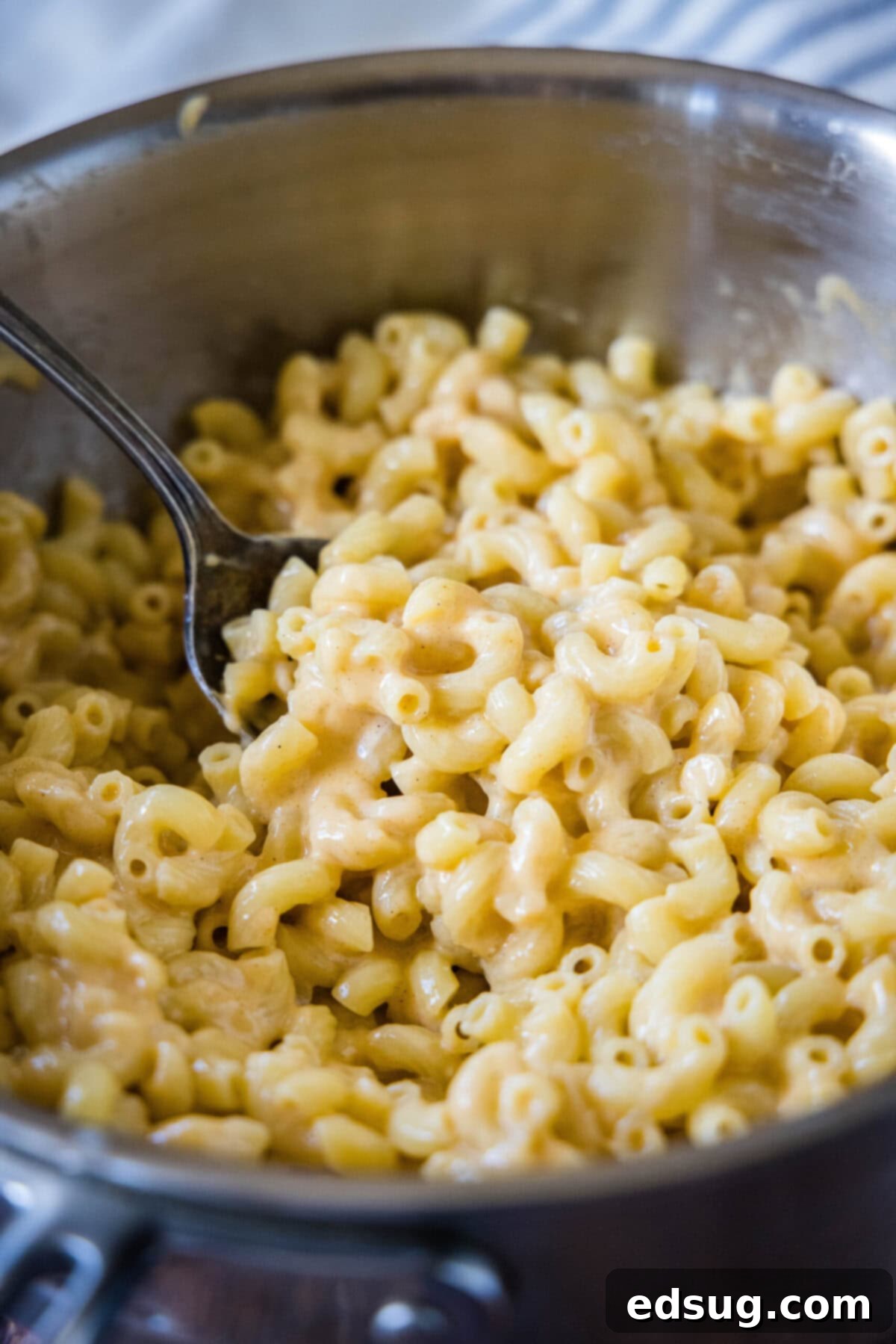 This easy and healthy mac and cheese, cooked on the stovetop, is loaded with protein-rich Greek yogurt, gooey melted cheese, and spicy seasonings, making it a delicious and mindful choice. A pot full of healthy mac and cheese with a serving spoon in it, ready to be dished out.