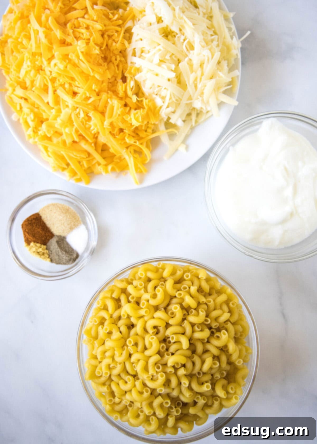 This easy and healthy mac and cheese on the stovetop is loaded with protein-rich Greek yogurt, gooey melted cheese, and spicy seasonings, made from these fresh and simple ingredients. Overhead view of the wholesome ingredients needed for healthy mac and cheese: a bowl of elbow macaroni, a bowl of freshly shredded Gruyere and sharp cheddar cheeses, a bowl of plain Greek yogurt, and a bowl containing garlic powder, ground mustard, paprika, freshly ground pepper, and sea salt.