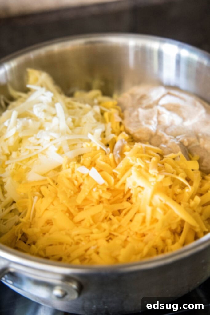 The essential components for this easy and healthy mac and cheese on the stovetop, featuring protein-rich Greek yogurt and two kinds of melted cheese. A bowl of shredded sharp cheddar and Gruyere cheeses next to a bowl of seasoned Greek yogurt, prepped for healthy mac and cheese.