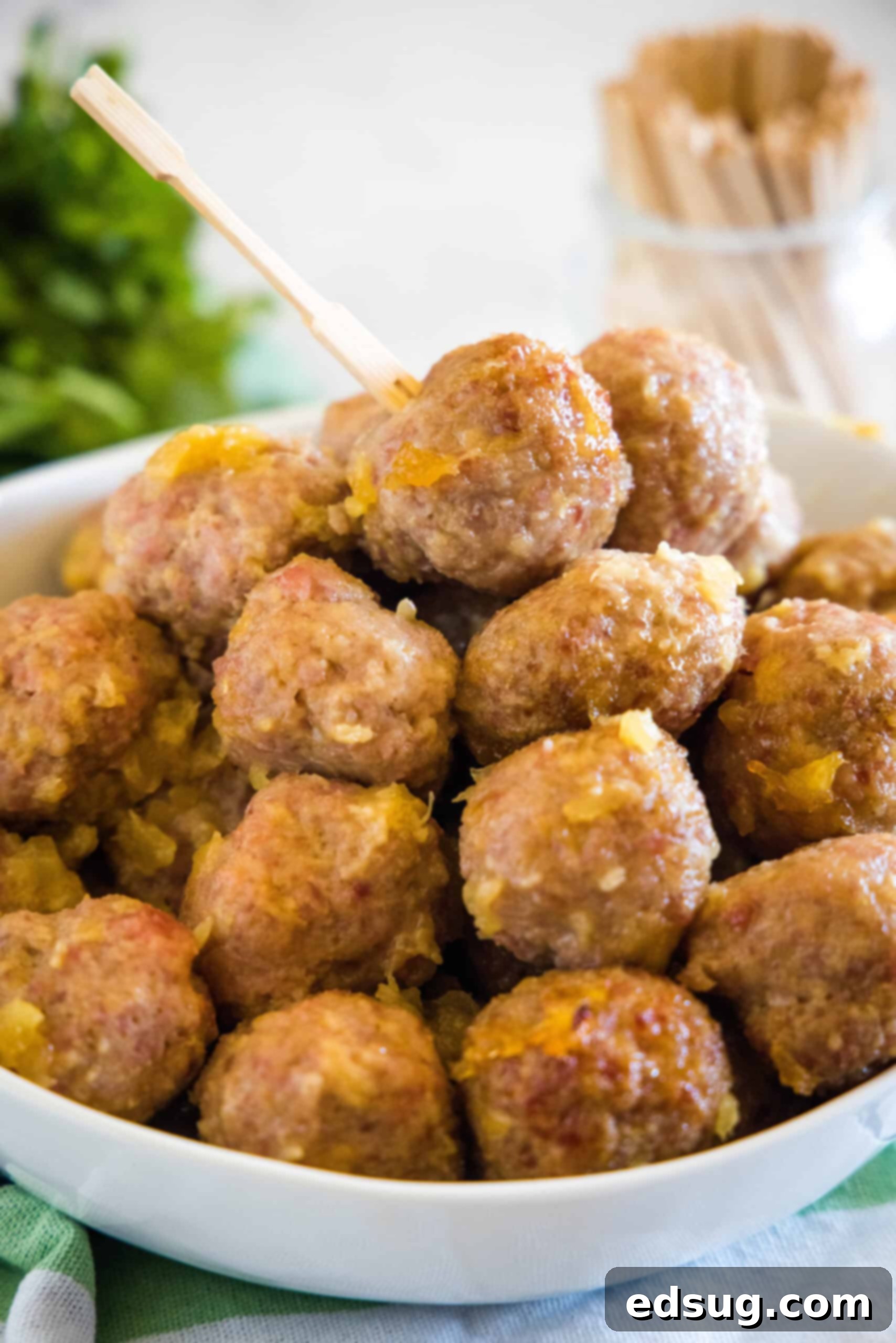 This ham balls recipe is the ultimate party snack! They're super juicy and easy to make. Bake them with two different sauces, sweet or savory! Ham balls with pineapple sauce piled into a bowl with a jar of cocktail skewers in the background.