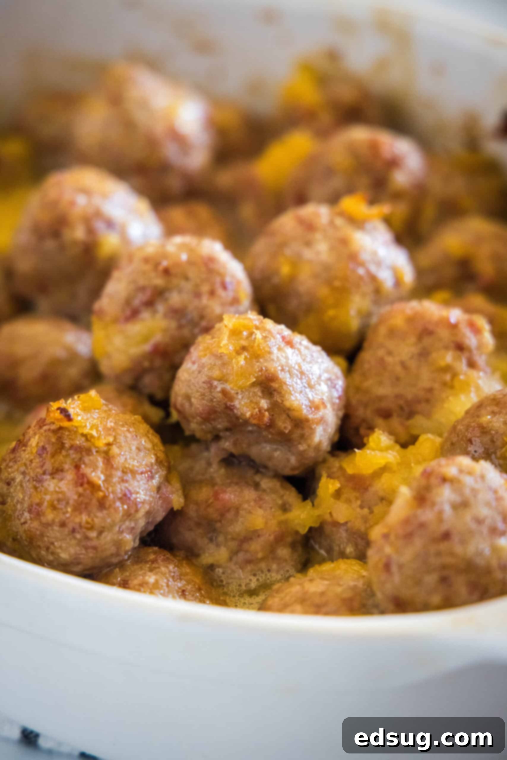 This ham balls recipe is the ultimate party snack! They're super juicy and easy to make. Bake them with two different sauces, sweet or savory! Close up of baked ham balls with pineapple sauce in a baking dish.