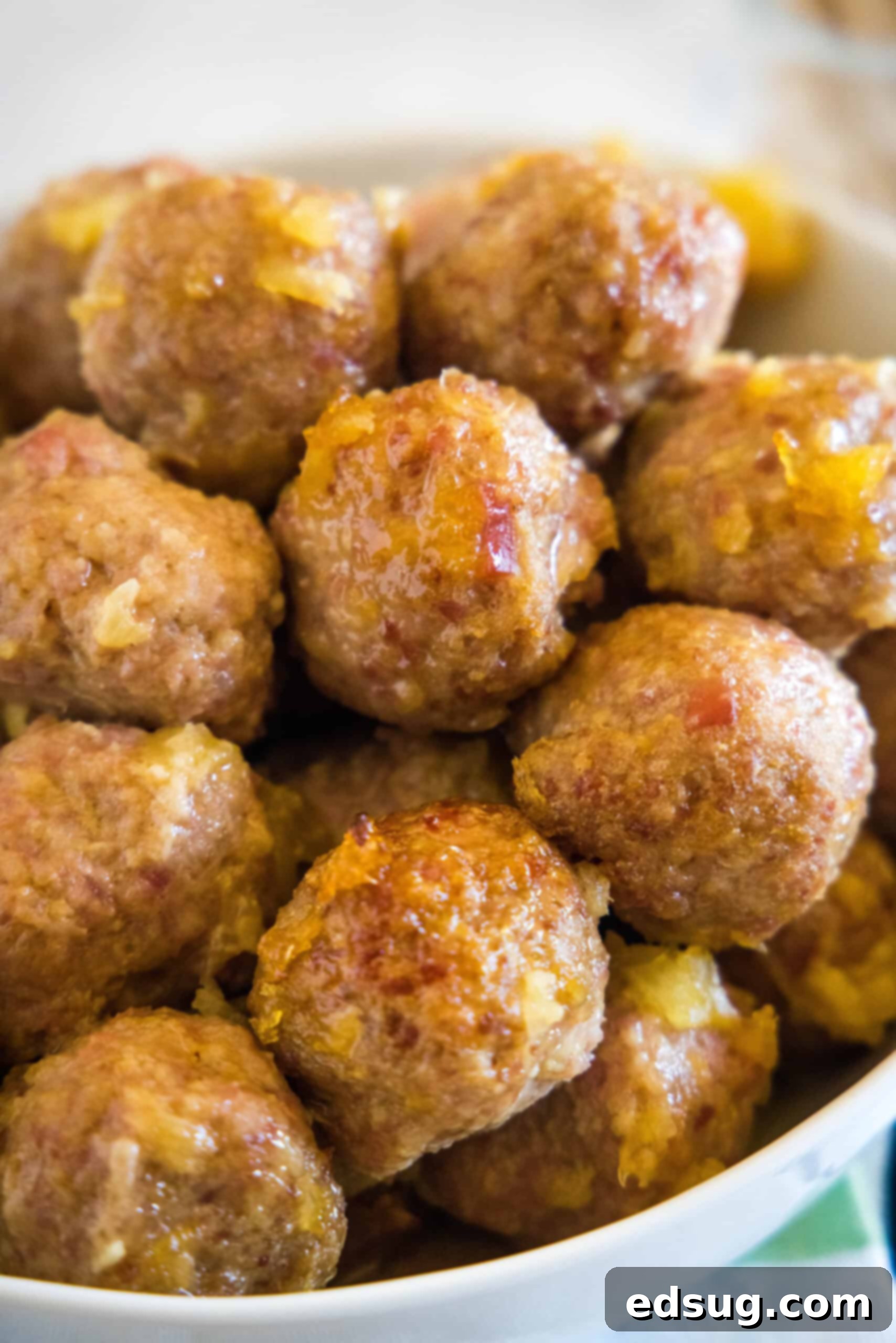 This ham balls recipe is the ultimate party snack! They're super juicy and easy to make. Bake them with two different sauces, sweet or savory! Ham balls with pineapple sauce piled into a bowl.