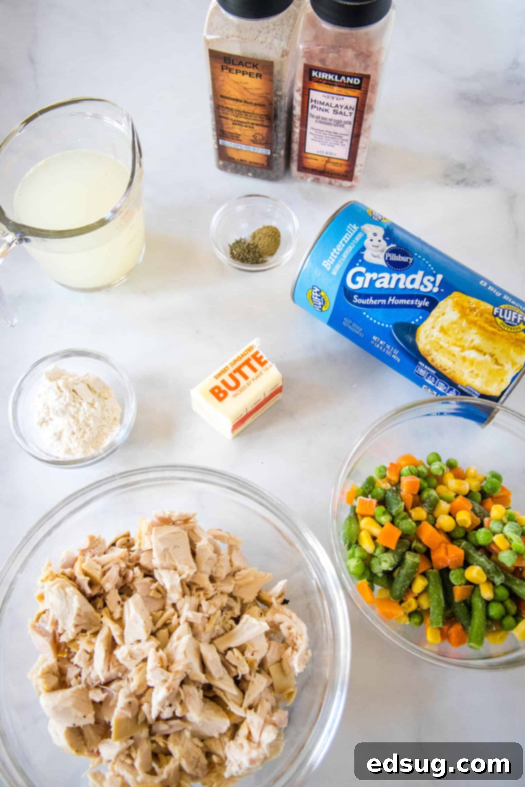 These mini chicken pot pies have creamy pot pie filling baked in a flaky biscuit crust. All the flavors of the original in bite-sized form! Ingredients for mini chicken pot pies laid out on a wooden surface, including canned biscuits, butter, flour, chicken broth, seasonings, mixed vegetables, and cooked chicken.