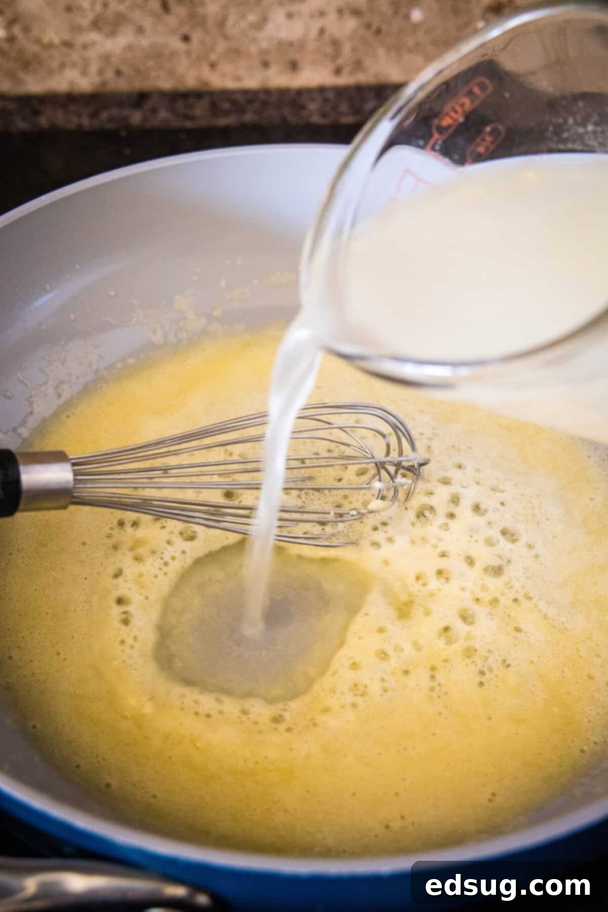 These mini chicken pot pies have creamy pot pie filling baked in a flaky biscuit crust. All the flavors of the original in bite-sized form! Chicken broth being poured into a roux of butter and flour in a skillet, creating the base for the creamy pot pie gravy.