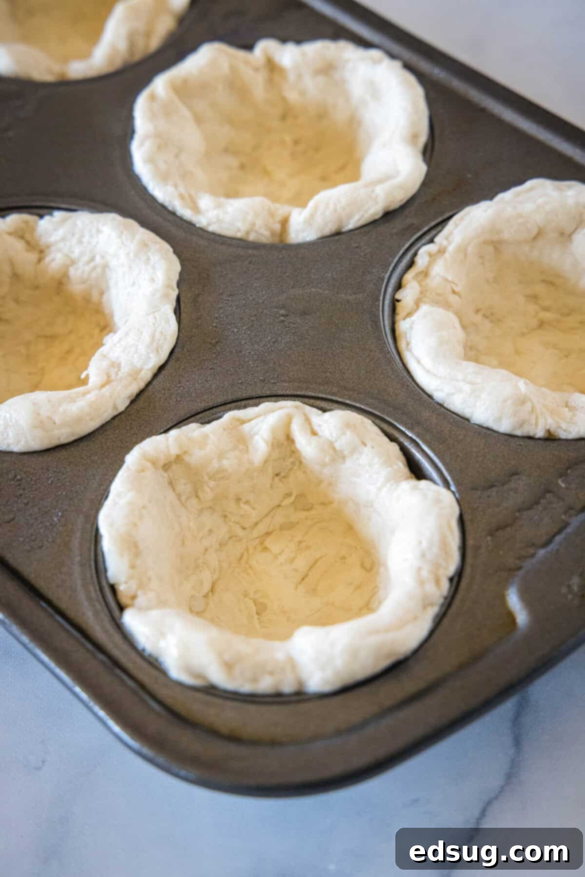These mini chicken pot pies have creamy pot pie filling baked in a flaky biscuit crust. All the flavors of the original in bite-sized form! Biscuit dough gently flattened and pressed into the wells of a muffin tin, forming individual mini pie crusts.