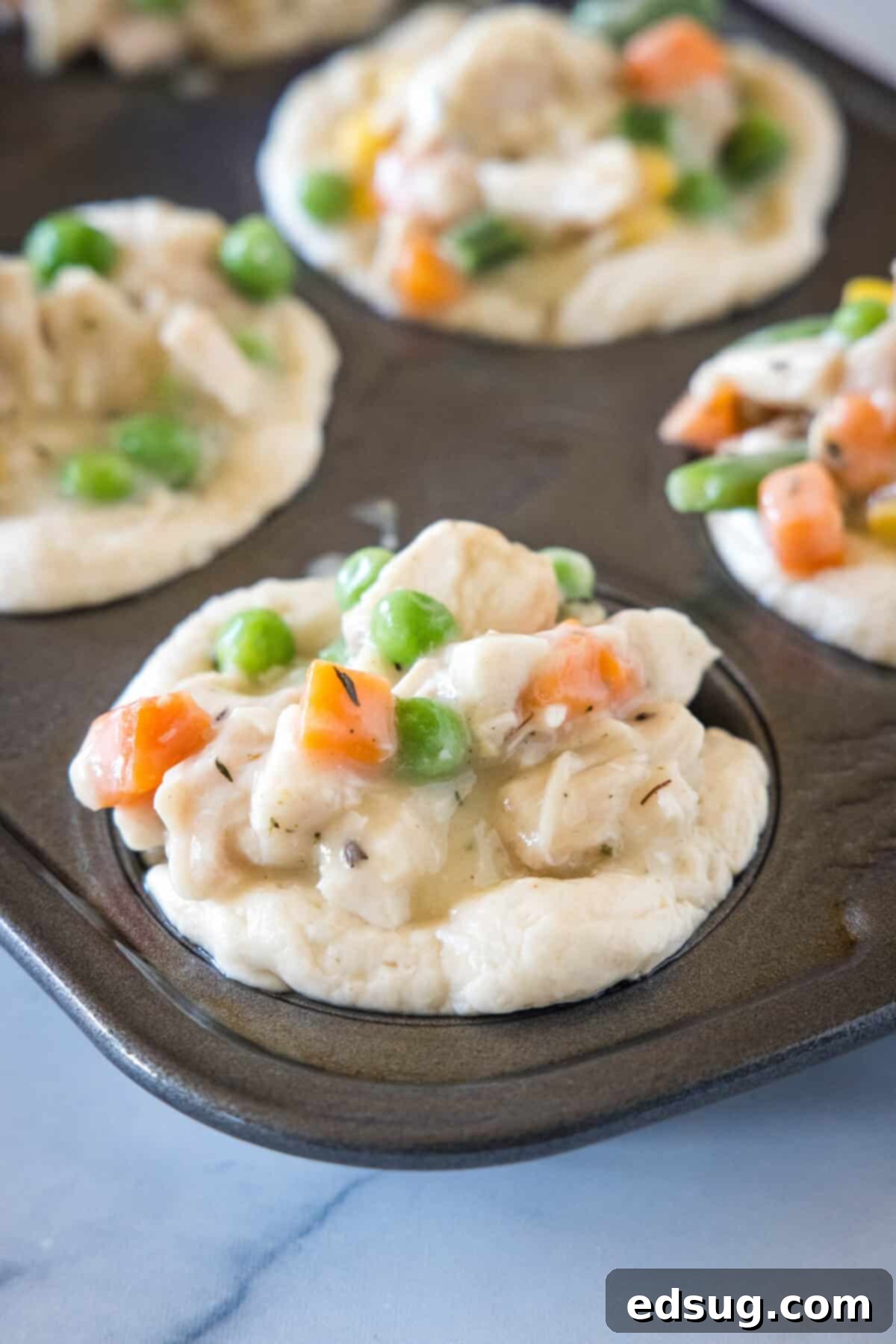These mini chicken pot pies have creamy pot pie filling baked in a flaky biscuit crust. All the flavors of the original in bite-sized form! Unbaked mini pot pies in a muffin tin, with creamy chicken and vegetable filling spooned into each biscuit crust.