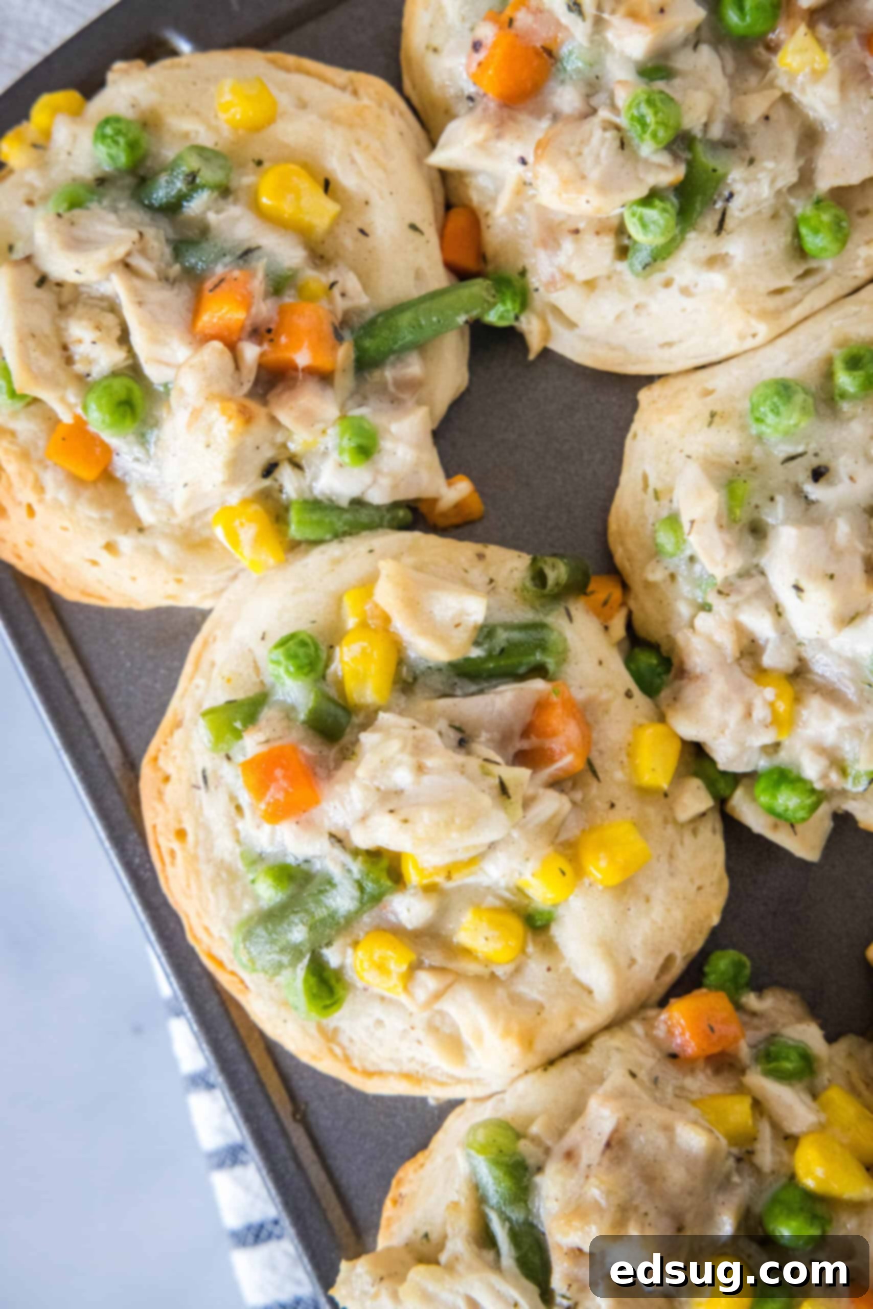 These mini chicken pot pies have creamy pot pie filling baked in a flaky biscuit crust. All the flavors of the original in bite-sized form! Overhead view of freshly baked mini chicken pot pies cooling in a muffin tin, showcasing their golden-brown biscuit crusts and bubbling filling.
