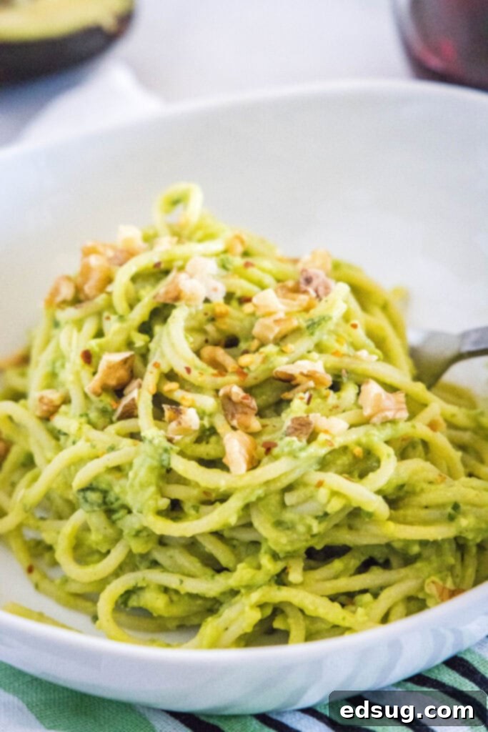 Velvety Avocado Dream Pasta 2 Creamy avocado pasta topped with chopped walnuts and red pepper flakes, served in a white bowl.