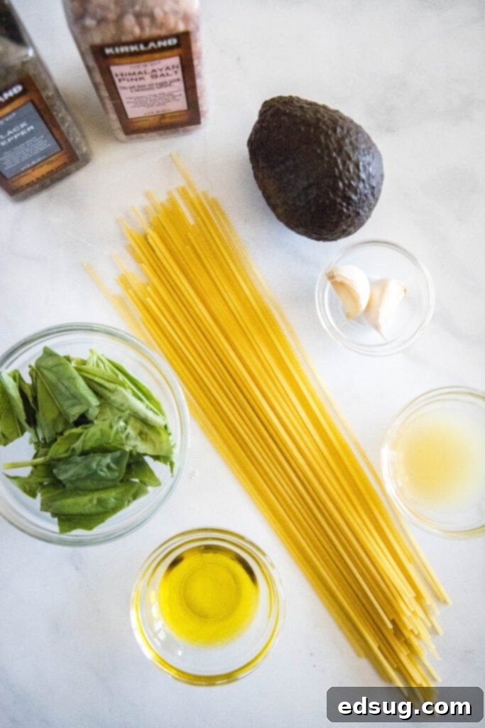 Velvety Avocado Dream Pasta 3 Ingredients for avocado pasta including whole avocados, fresh basil, lime, garlic, and a bottle of olive oil arranged on a kitchen counter.