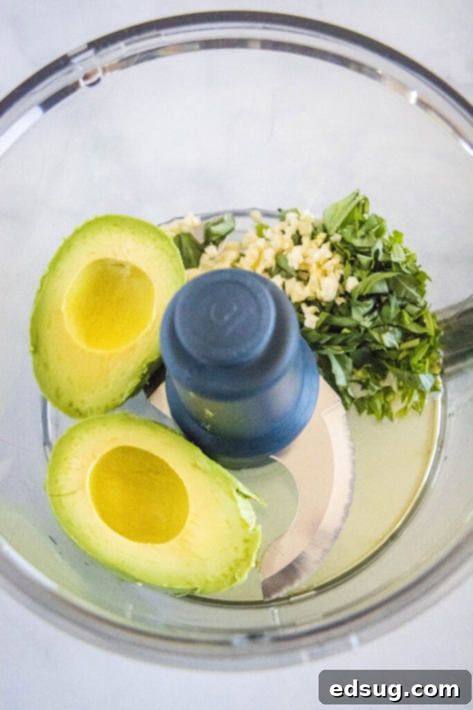 Velvety Avocado Dream Pasta 4 Ripe avocado, fresh basil leaves, and garlic cloves being added to a food processor bowl, ready to be blended into a sauce.
