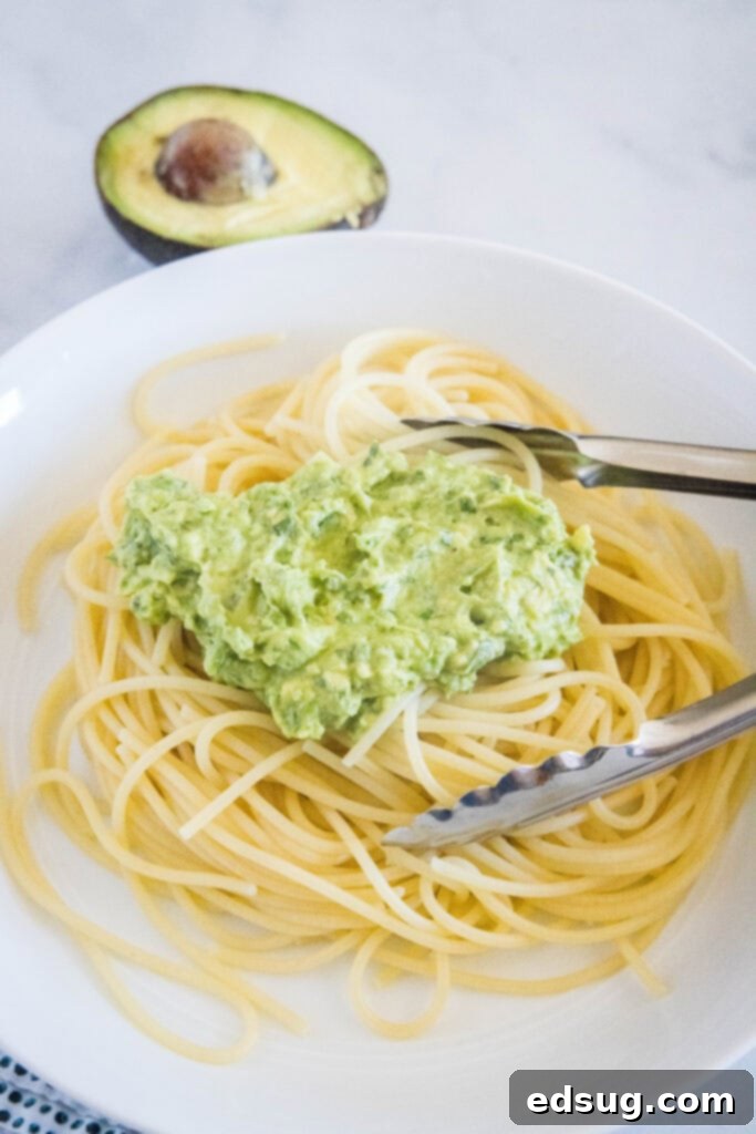 Velvety Avocado Dream Pasta 5 Cooked spaghetti being transferred to a bowl, with the creamy green avocado sauce already in the bowl, ready for tossing.