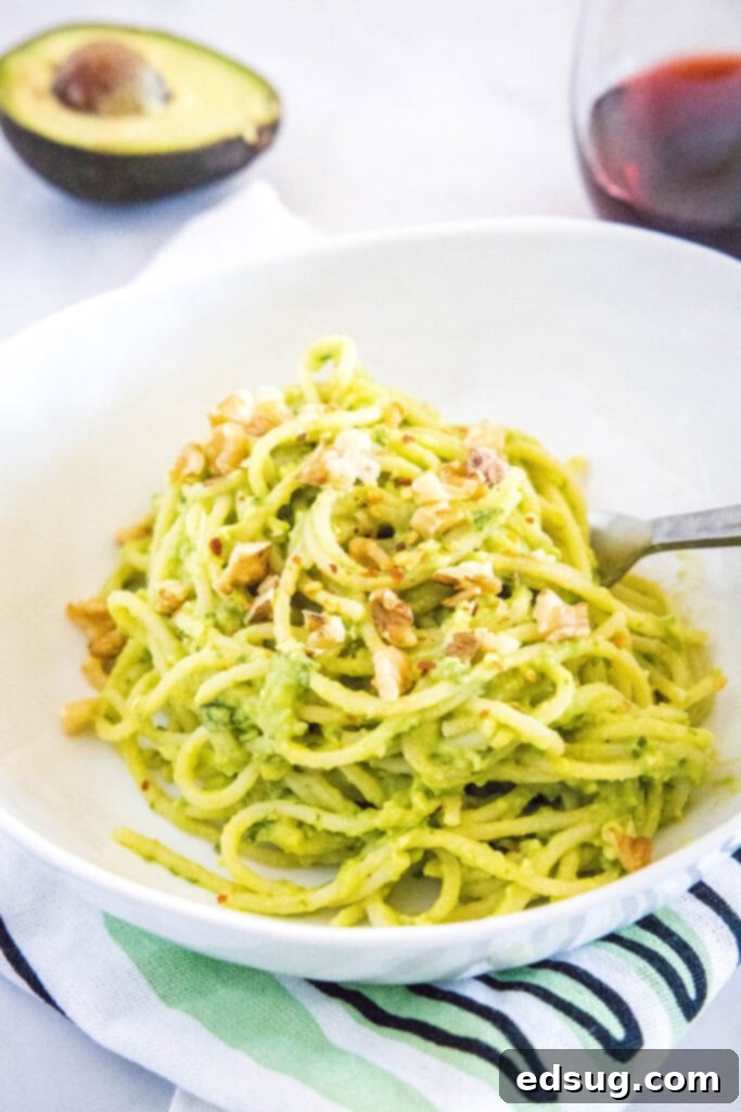 Velvety Avocado Dream Pasta 6 Overhead view of creamy avocado pasta in a bowl, generously topped with chopped walnuts and a hint of red pepper flakes.