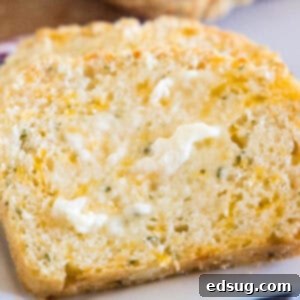 Close up of a slice of cheesy quick bread spread with butter, highlighting the soft interior and golden crust, making it look irresistible.