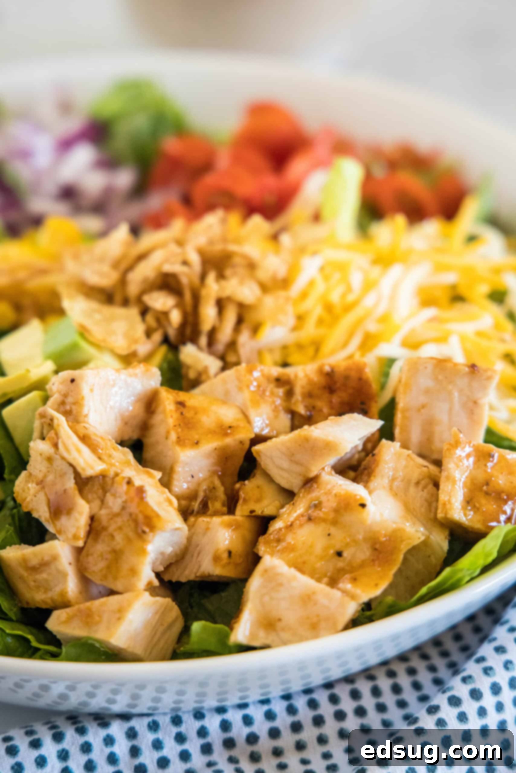 This BBQ chicken salad has juicy bites of sweet-smoky chicken tossed with tomatoes, avocado, and sweet corn in creamy barbecue ranch dressing. A vibrant BBQ chicken salad in a white bowl, showcasing the colorful mix of ingredients like chopped chicken, fresh greens, grape tomatoes, corn, and avocado, ready to be enjoyed.