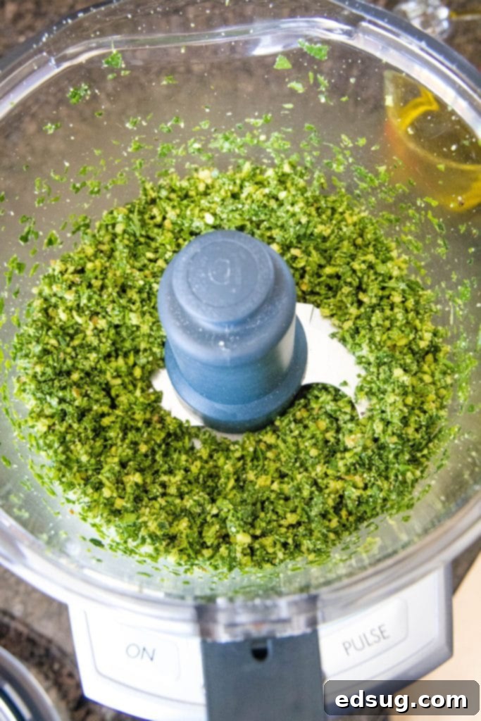 Overhead view of spinach, basil, garlic, and parmesan cheese chopped up in a food processor