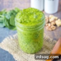 A jar of pesto with spinach and walnuts in the background