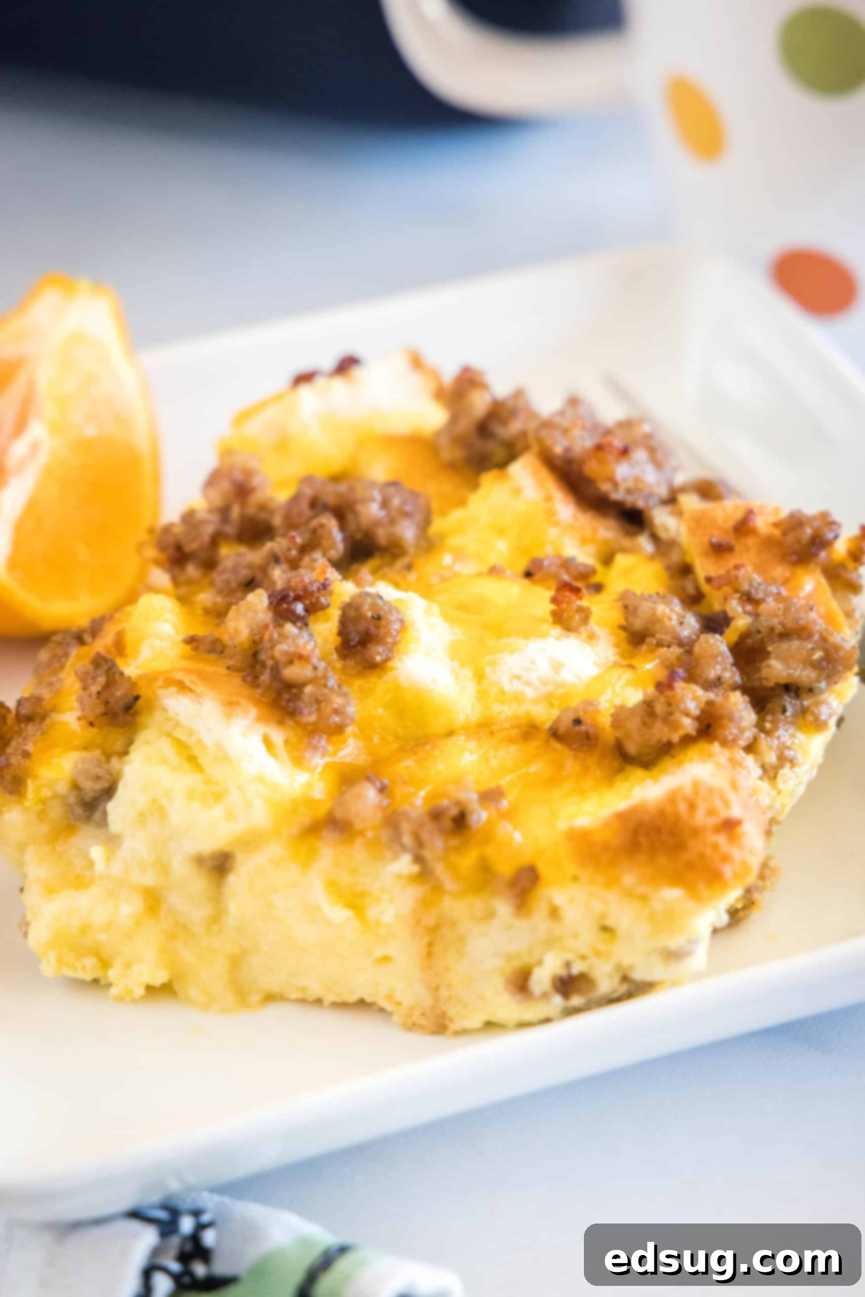 This sourdough breakfast casserole is the ultimate make-ahead breakfast packed with sourdough bread chunks, breakfast sausage, and cheese! A delicious serving of sourdough breakfast casserole on a white plate, garnished with fresh orange slices and a fork, highlighting its golden-brown top and melted cheese.