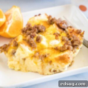 A serving of sourdough breakfast casserole next to orange slices and a fork on a white square plate.