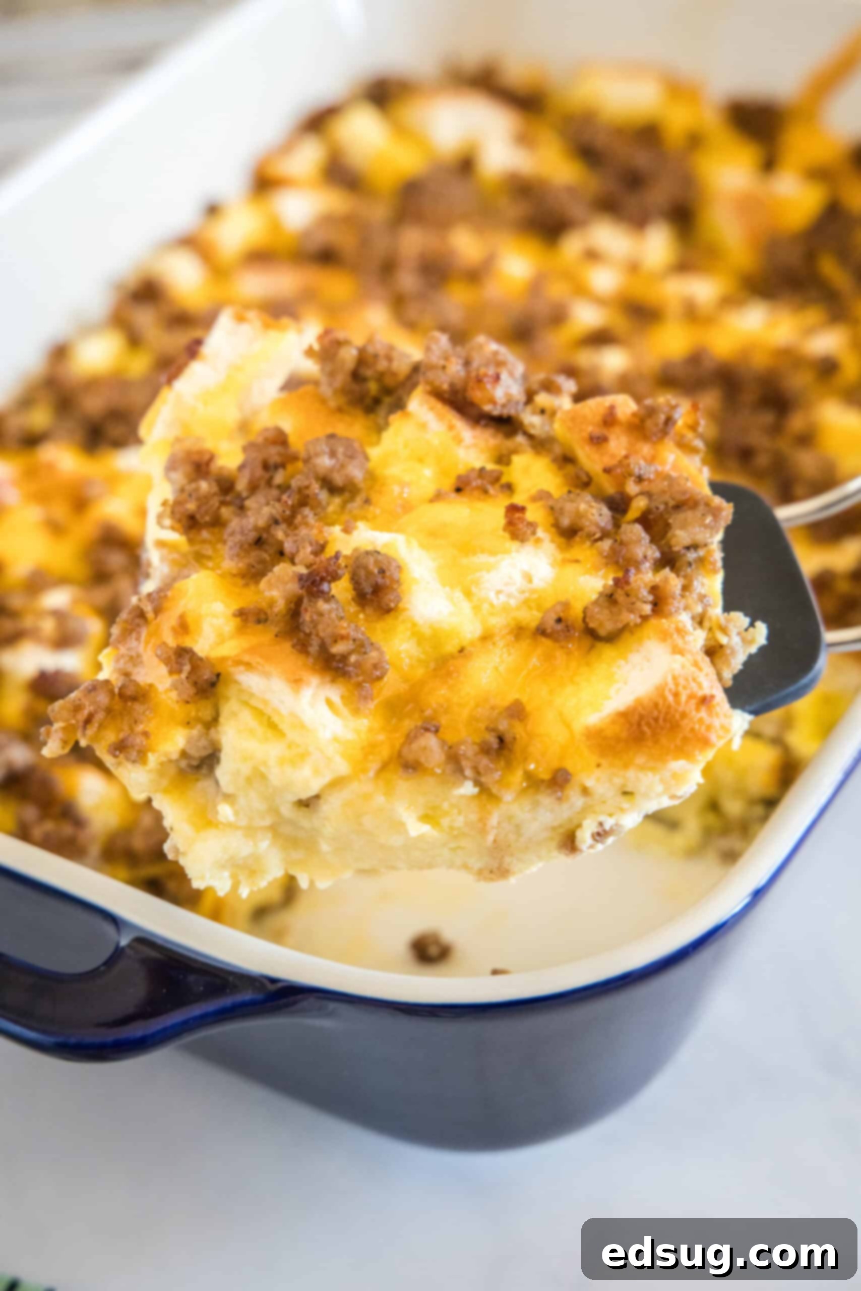 This sourdough breakfast casserole is the ultimate make-ahead breakfast packed with sourdough bread chunks, breakfast sausage, and cheese! A spatula lifting a generous serving of hot, cheesy sourdough breakfast casserole from a baking dish, ready to be enjoyed.