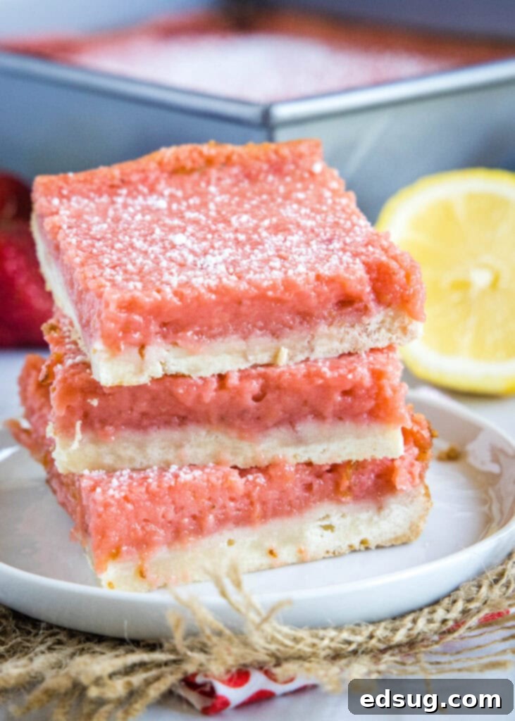 Bright & Tangy Strawberry Lemonade Treats 2 Perfectly stacked strawberry lemon bars dusted with powdered sugar on a white plate, showcasing their vibrant pink filling and crumbly shortbread crust.